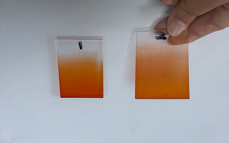 Hand holding two pieces of orange gradient frosted acrylic plate sample against white background