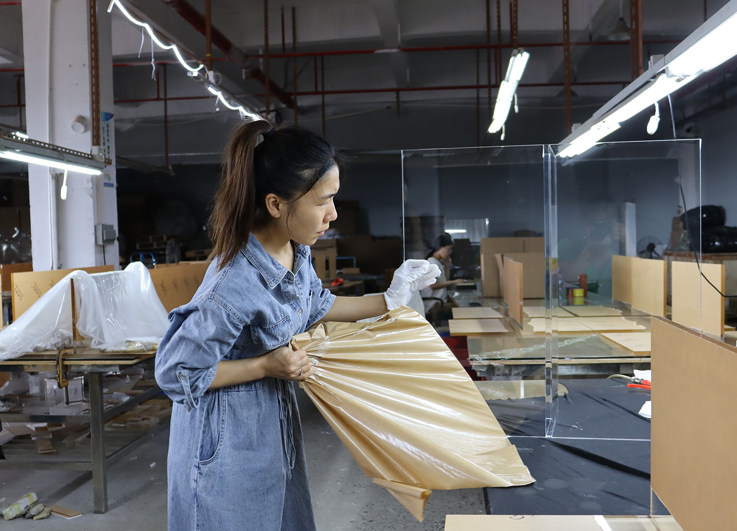 Female production worker wrapping bubble padding around acrylic pet enclosure semi-finished goods