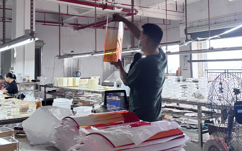 Factory staff inspecting finished gradient orange acrylic side table before packaging