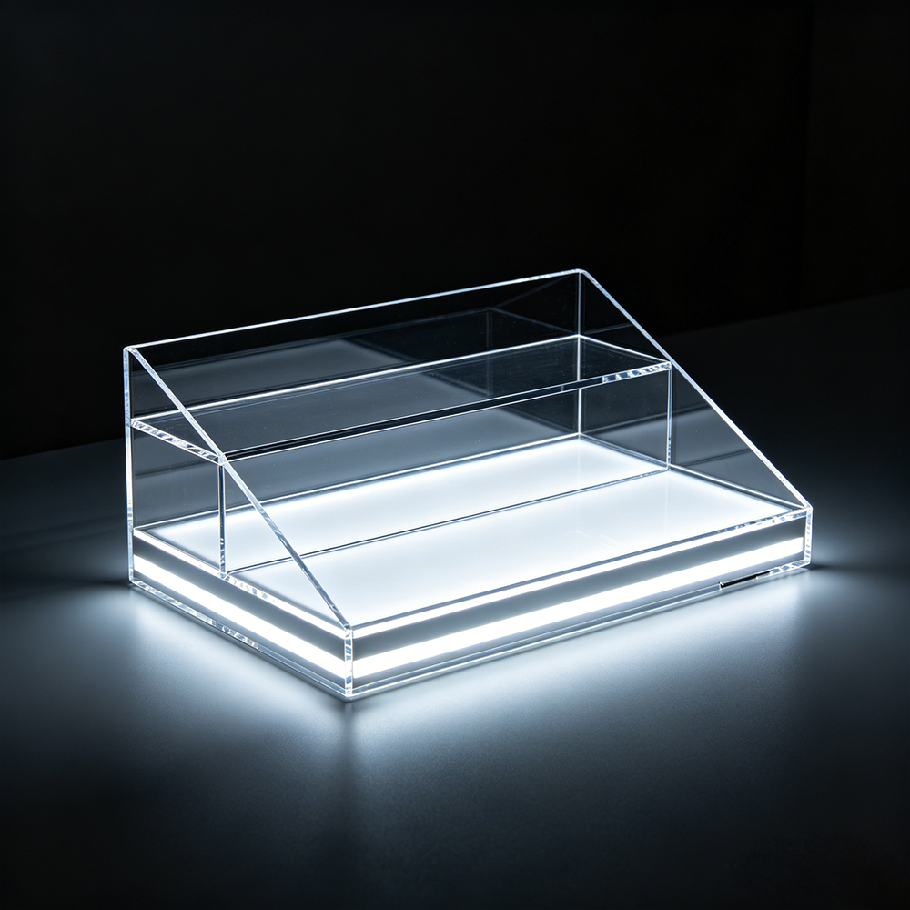 Sloped front low-profile transparent acrylic tiered display stand with built-in base LED lighting, dark gray studio backdrop for retail merchandise
