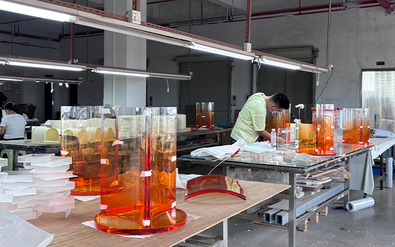 Workers processing gradient orange transparent acrylic cylindrical furniture at factory workstations