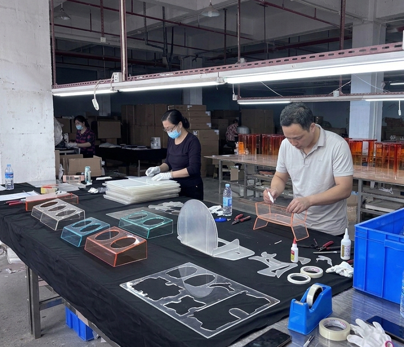 Workers processing acrylic pet bowl and pet enclosure raw panels at production bench in acrylic manufacturing plant