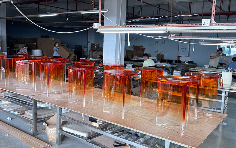 Factory workshop batch production of gradient orange transparent acrylic side tables, workers assembling finished furniture