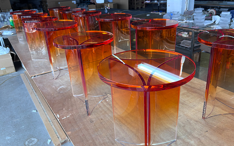 Stacked finished gradient orange transparent acrylic curved coffee tables inside manufacturing workshop