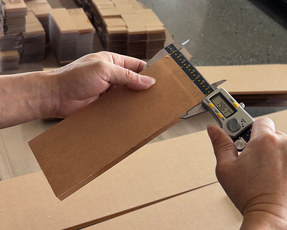 Worker measuring brown protective paper acrylic template with digital caliper for size inspection