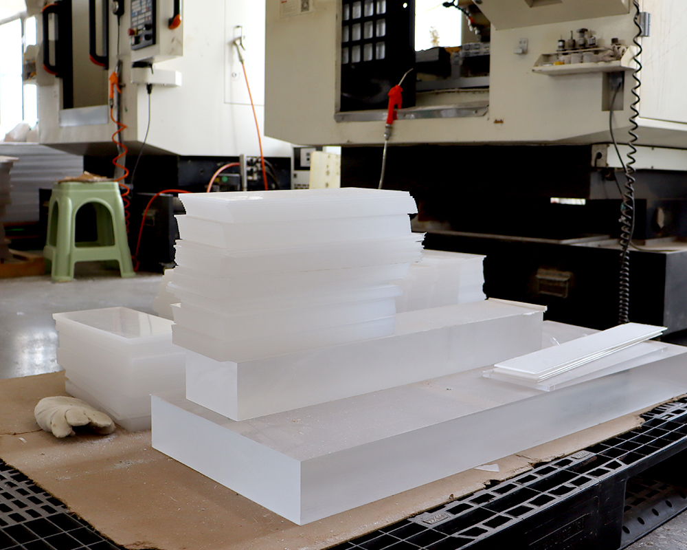 Acrylic factory workshop, stacked thick frosted white acrylic raw material blocks beside CNC cutting machine