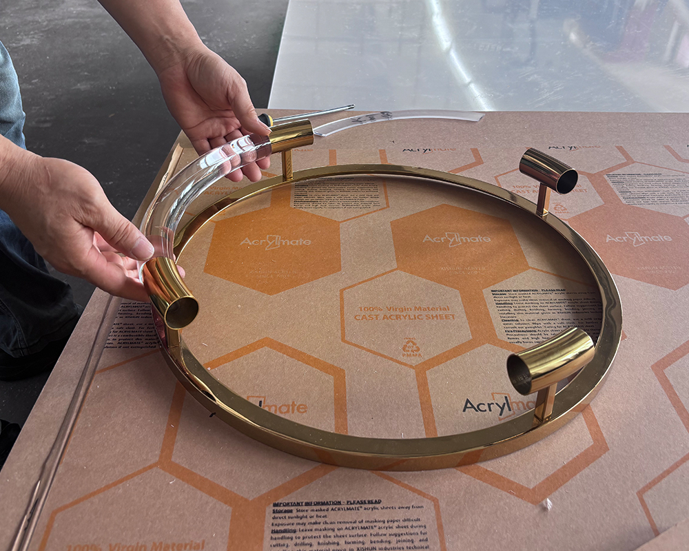 Worker assembling round acrylic serving tray with brass metal handles, honeycomb protective paper base