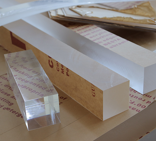 Heavy-gauge clear acrylic blocks and thick lucite slabs with kraft paper masking, 100% virgin MMA optical-grade material for custom furniture fabrication.