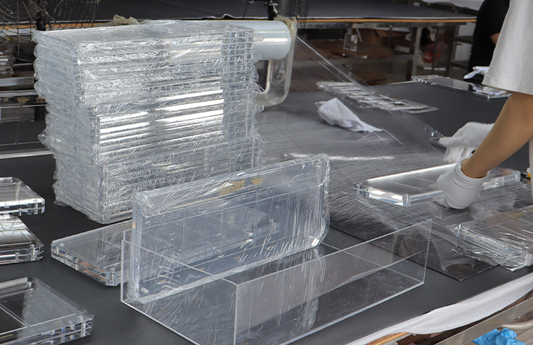 Workers packaging clear acrylic display boxes and panels with protective film