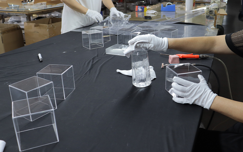 Worker Cleaning and Inspecting Clear Acrylic Display Boxes on a Quality Control Table