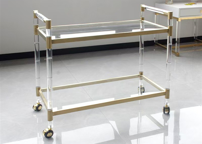 Stainless steel medical instrument trolley with two glass shelves and caster wheels in a hospital room.