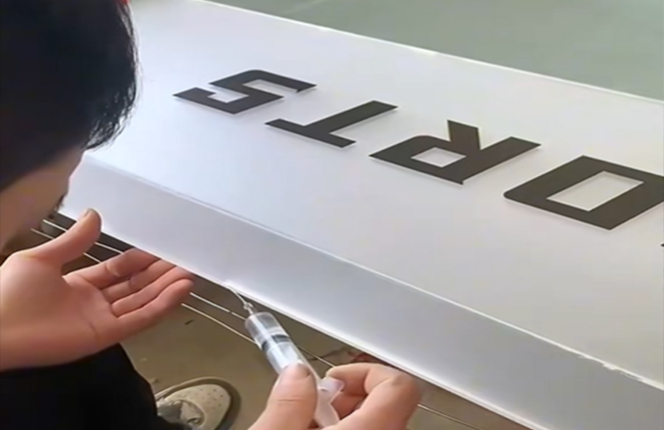 worker applying adhesive to raised black letters on a white acrylic sign panel