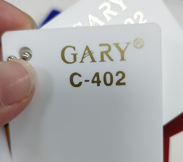 Hand holding a GARY brand pure white acrylic material color swatch sample card labeled C-402 with gold lettering.